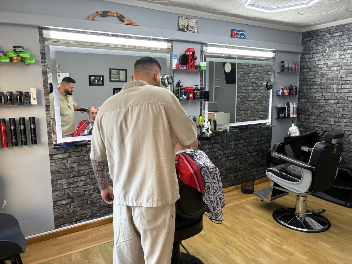 Interior de Barberia Rigo con un barbero atendiendo, espejos y sillones de barbería